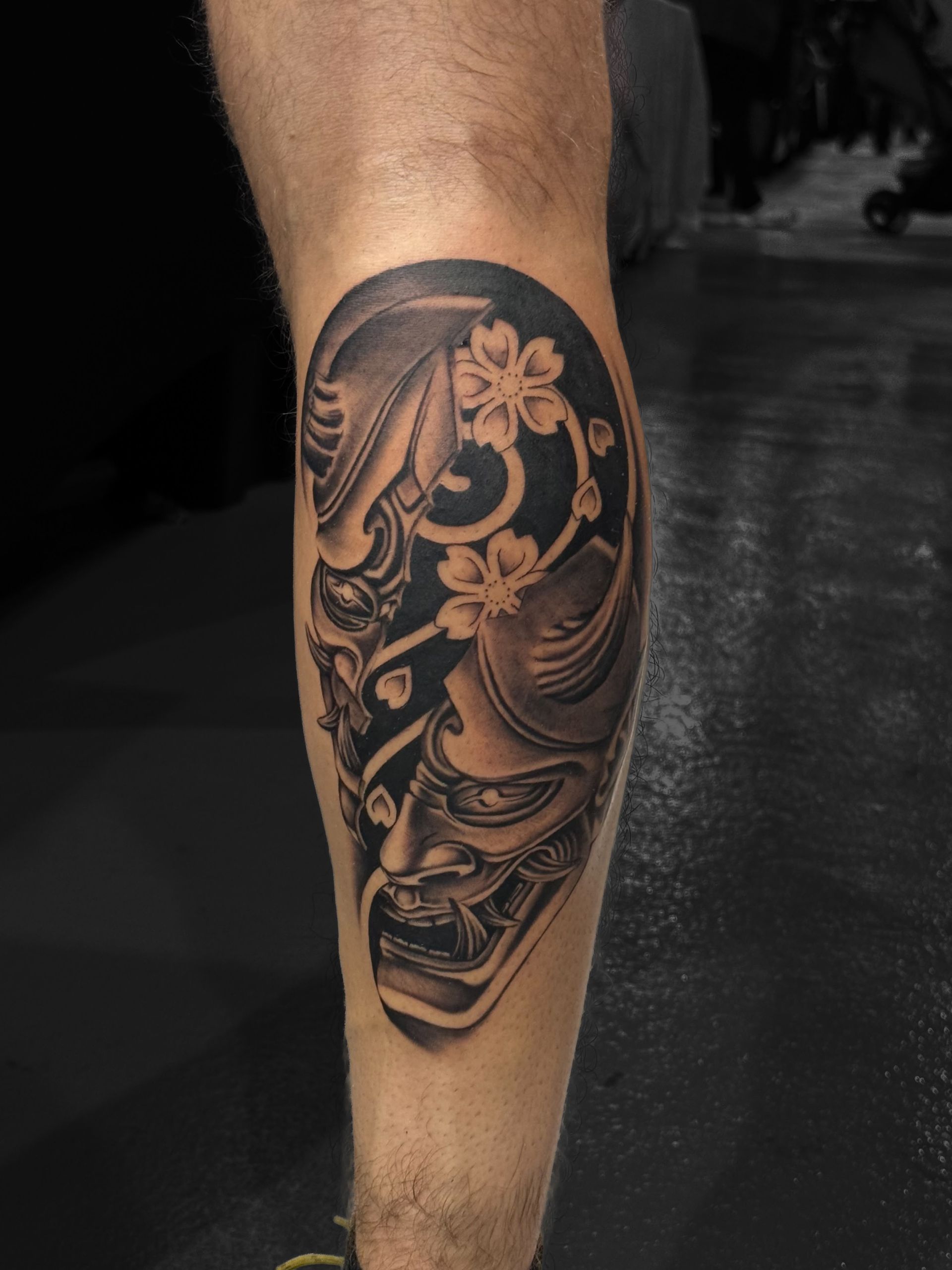 A detailed black-and-grey tattoo on a forearm featuring an angel statue figure with wings above geometric shadow shapes.