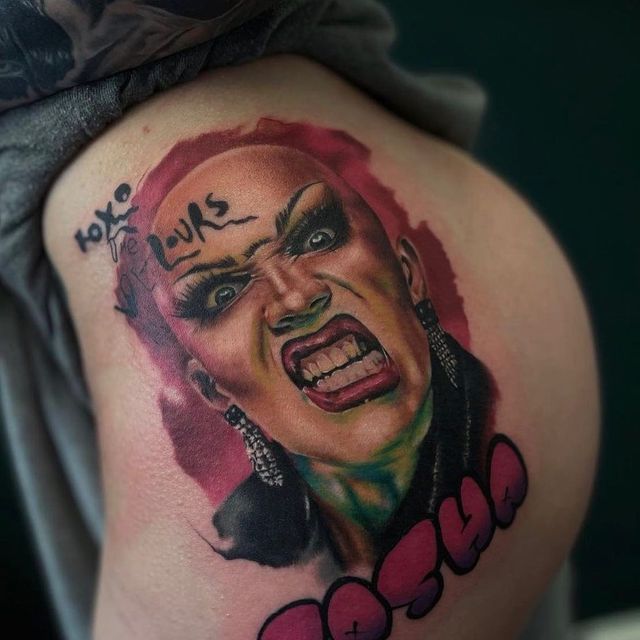 A tattoo on skin depicting a person with a fierce expression, dramatic makeup, and the words 